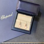 Chopard blue jewelry box open to reveal pink heart-shaped earrings in a beige display tray.
