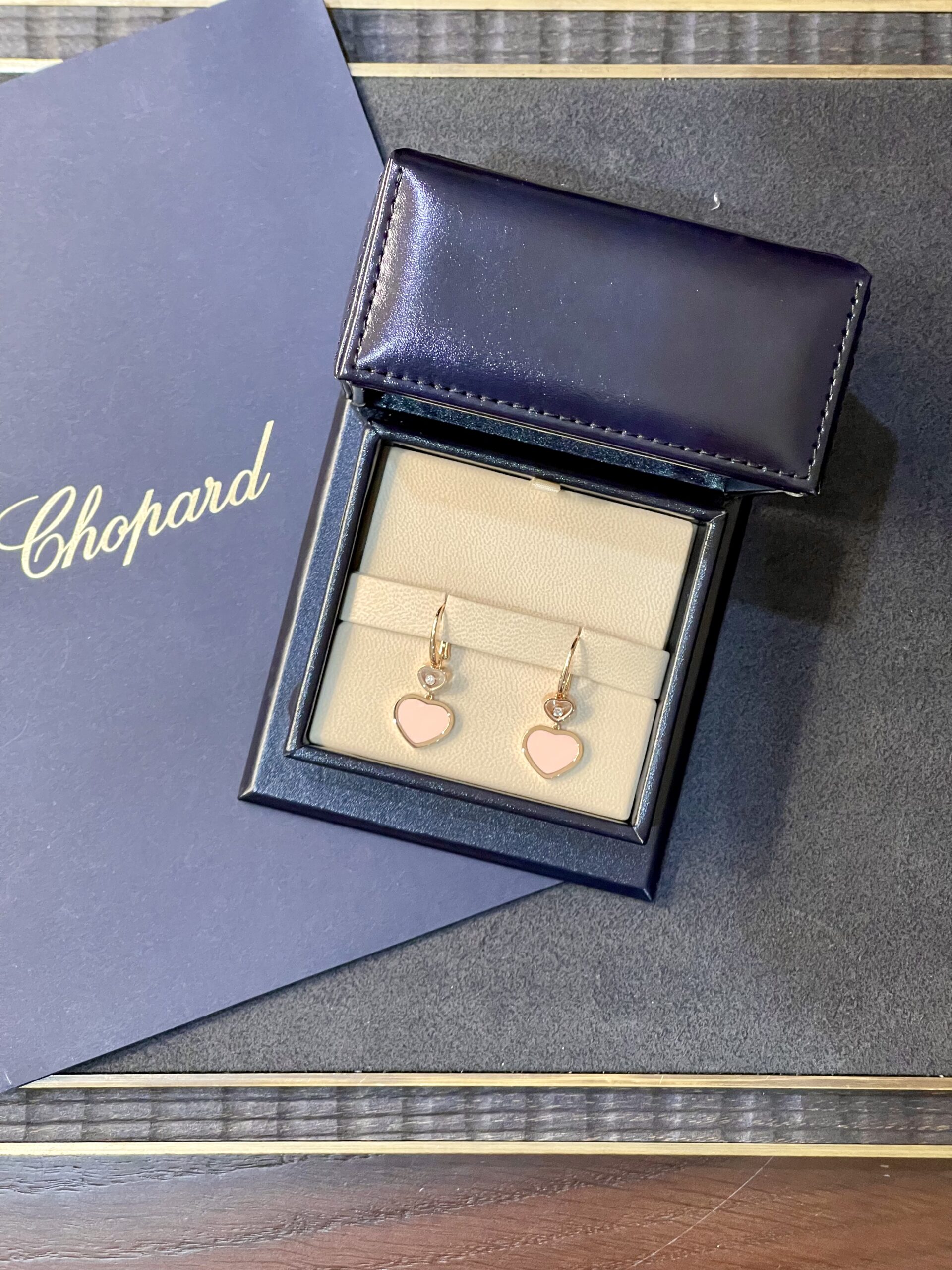 Chopard blue jewelry box open to reveal pink heart-shaped earrings in a beige display tray.