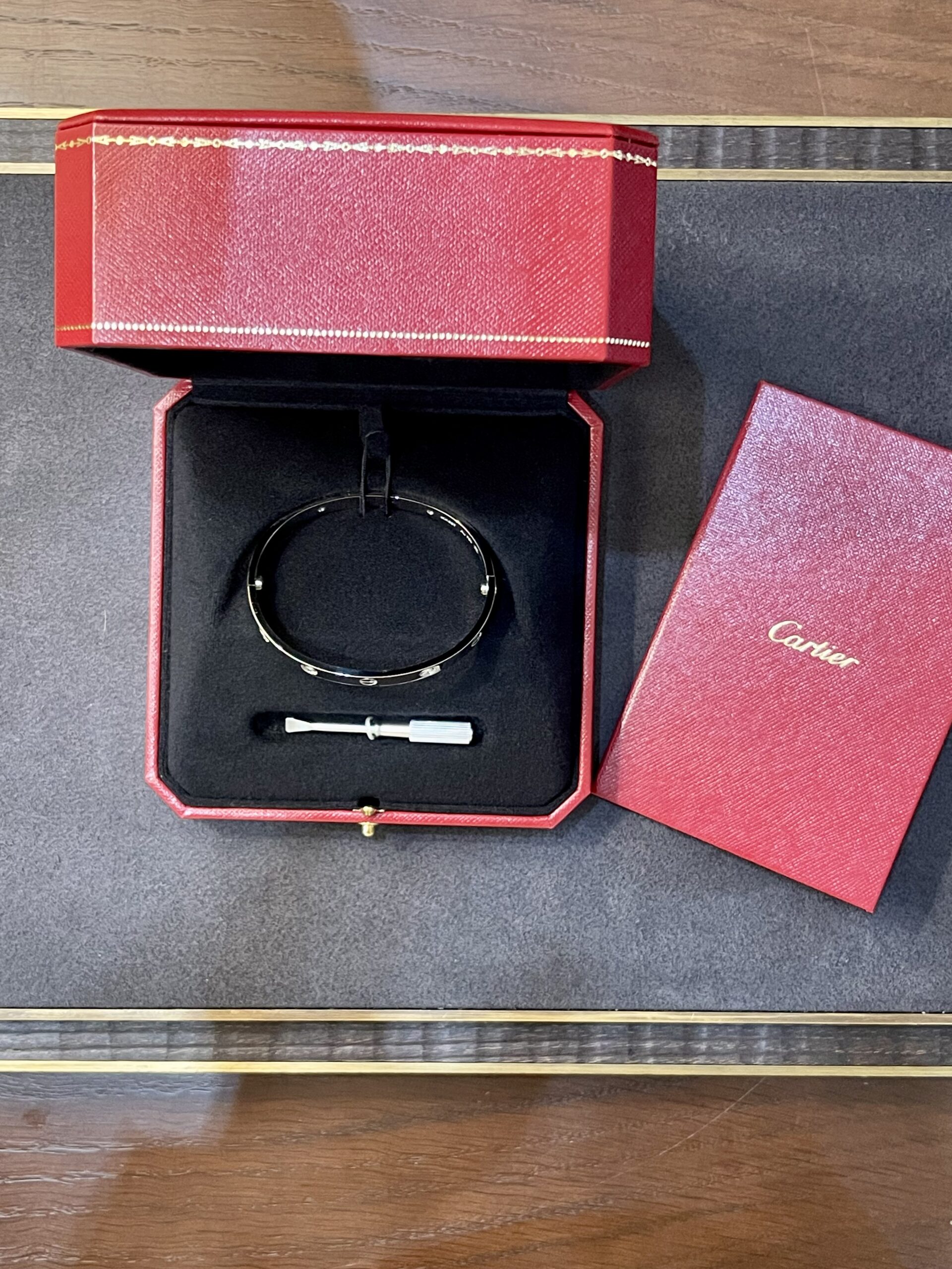 Red Cartier jewelry box opened to reveal a bracelet in black velvet tray, with a small tool resting beneath it
