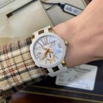 Wrist wearing a white and gold Ulysse Nardin watch with a mother-of-pearl dial and roman numerals, over a plaid sleeve