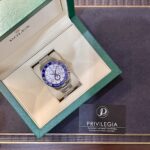 Opened green Rolex box displaying a silver Yacht-Master watch with a blue bezel on a beige insert; Privilegia card nearby.