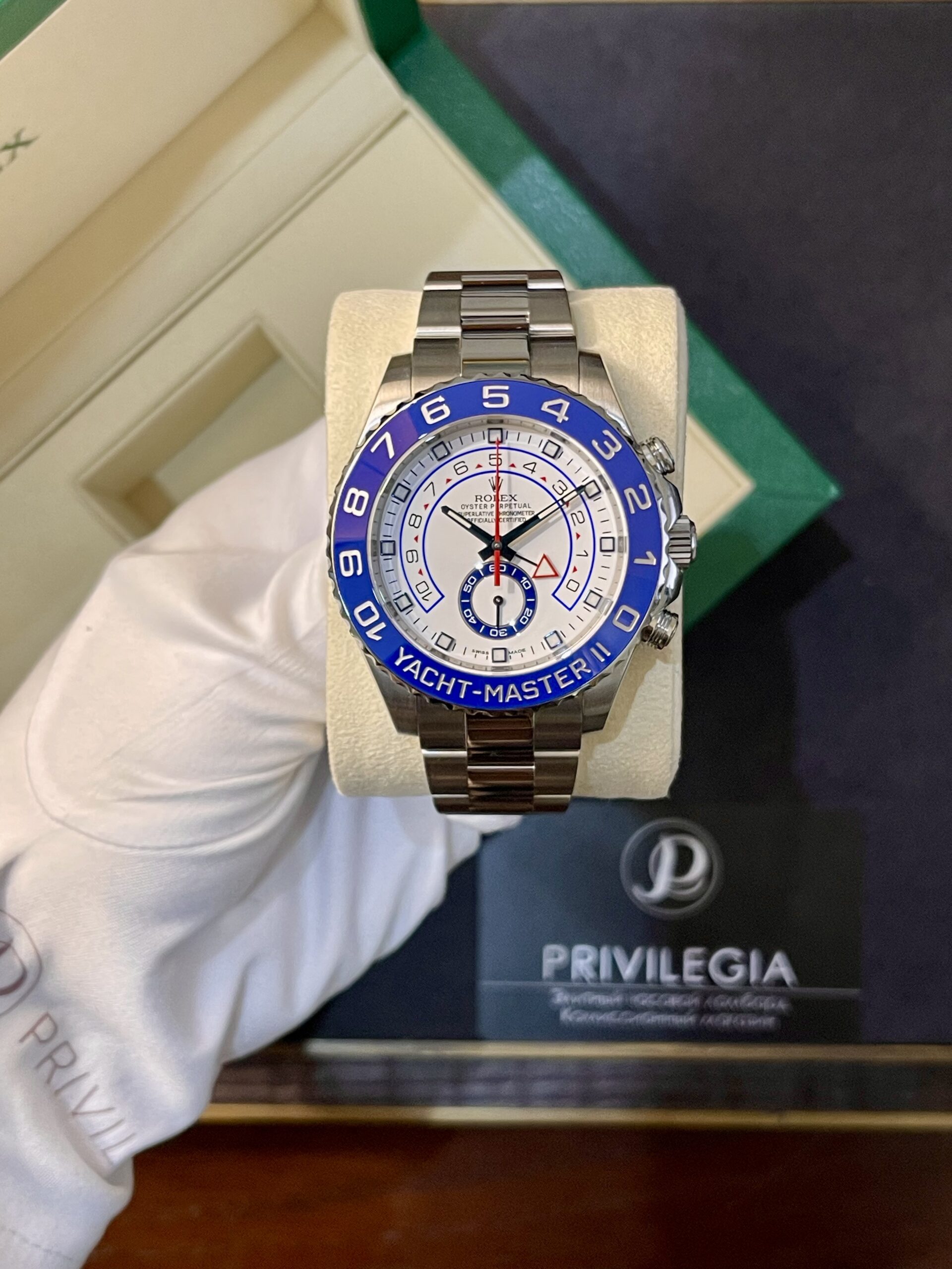 Stainless steel Rolex wristwatch with blue bezel reading YACHT-MASTER II, displayed on a beige cushion box.
