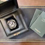 Luxurious Audemars Piguet watch in an open black presentation box with green manuals nearby on a wooden surface