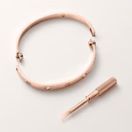Rose gold Cartier Love bracelet with screw accents, shown with a small matching screwdriver tool beside it.