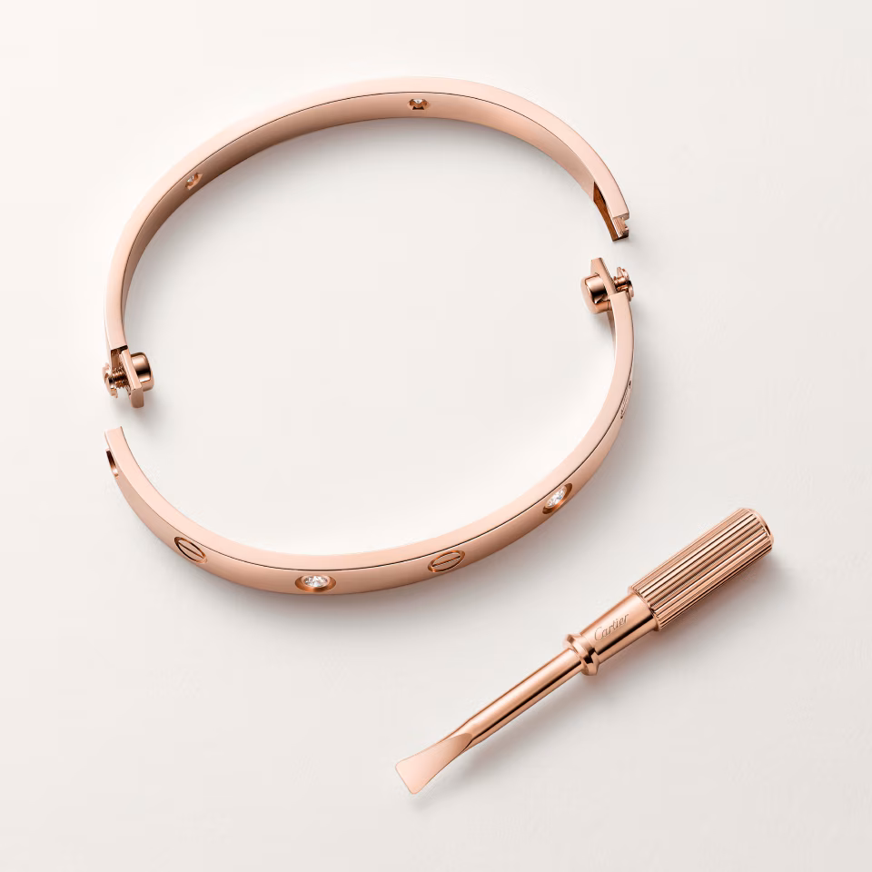 Rose gold Cartier Love bracelet with screw accents, shown with a small matching screwdriver tool beside it.