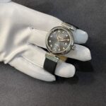 Close-up of a stainless steel wristwatch with a black sunburst dial and diamond hour markers held by a gloved hand.