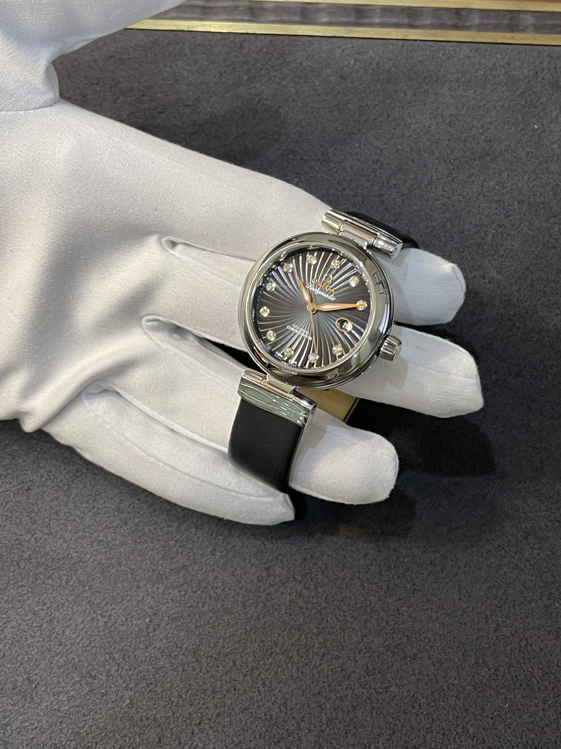 Close-up of a stainless steel wristwatch with a black sunburst dial and diamond hour markers held by a gloved hand.