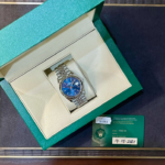 Rolex watch with a blue dial in a green presentation box and accompanying certificate showing 14-05-2021 date of purchase, stainless steel bracelet visible.