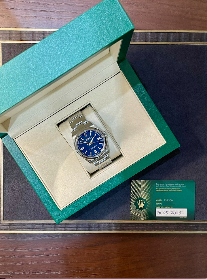 Rolex stainless steel watch with a blue dial in an open green presentation box, with a green warranty card nearby.