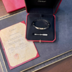 Cartier bracelet in an open red presentation box with a certificate nearby on a wooden surface.