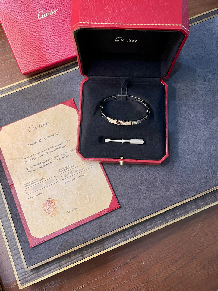 Cartier bracelet in an open red presentation box with a certificate nearby on a wooden surface.