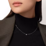 Close-up of a woman wearing a delicate silver necklace with a small bead pendant over a black turtleneck and brown pinstripe blazer.