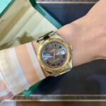 Two-tone Rolex Datejust on a striped orange and white shirt sleeve, with a green box in the background.