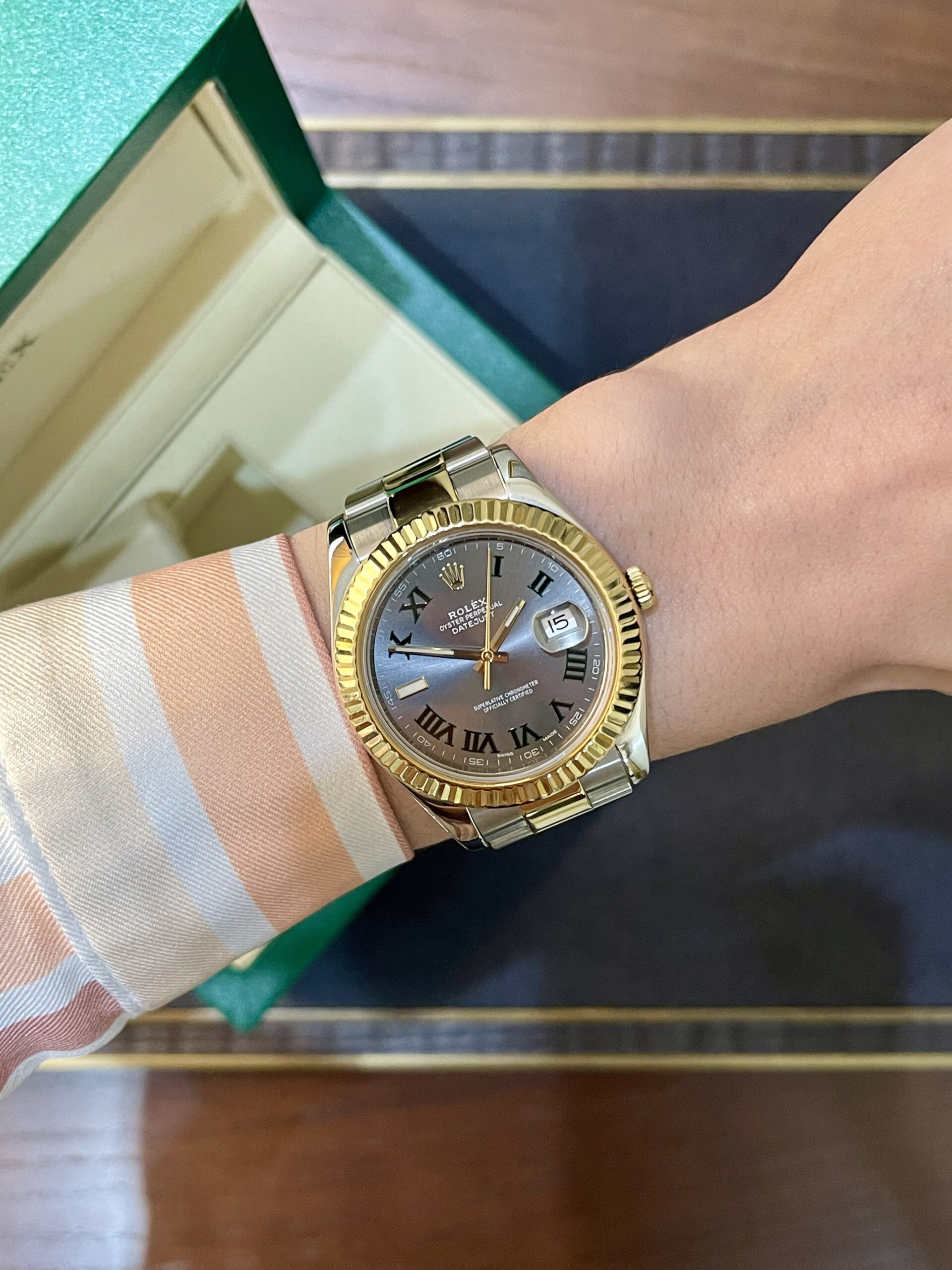 Two-tone Rolex Datejust on a striped orange and white shirt sleeve, with a green box in the background.