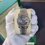 Rolex Datejust stainless steel watch with Roman numeral dial in a green box, held by gloved hand.