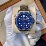 Omega Seamaster diver watch with a blue dial and stainless steel bracelet displayed on a cream cushion in a box.