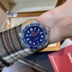 Wrist wearing a blue Omega Seamaster diver's watch with a stainless steel bracelet, plaid sleeve visible in the foreground.